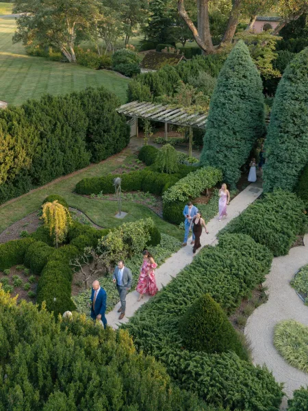 Garden wedding venue featuring a pergola beside a lawn, an outdoor garden venue framed by trees and garden beds.