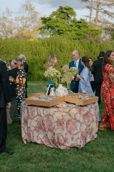 Cocktail hour setup for an outdoor cocktail hour on a lawn, highlighted by hydrangeas, with hedges and trees under an open sky.