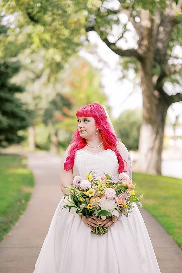 Bridal portrait of a bride holding bouquet in a white strapless gown with veil and pearl necklace on a park pathway among trees