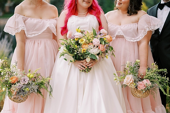 Bridesmaid portraits with bride with bridesmaids in blush off-the-shoulder dresses, one holding a colorful bouquet in a garden setting