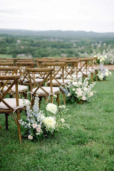 Ceremony aisle decor with outdoor ceremony aisle lined by low white and pastel florals and greenery beside cross back chairs, mountain view beyond