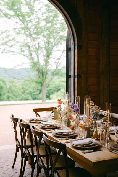 Reception tablescape on a wood farm table wedding reception with woven chargers, linen napkins, taper candles, bud vase florals and citrus accents