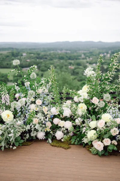 Ceremony floral installation with grounded ceremony florals of roses, peonies, delphinium and greenery on a wood deck with rolling hills behind
