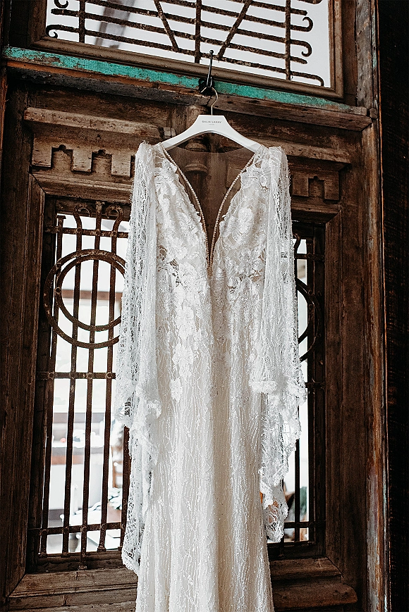 Wedding dress, lace wedding dress with deep V illusion neckline and long sleeves hanging on a door with iron window grille