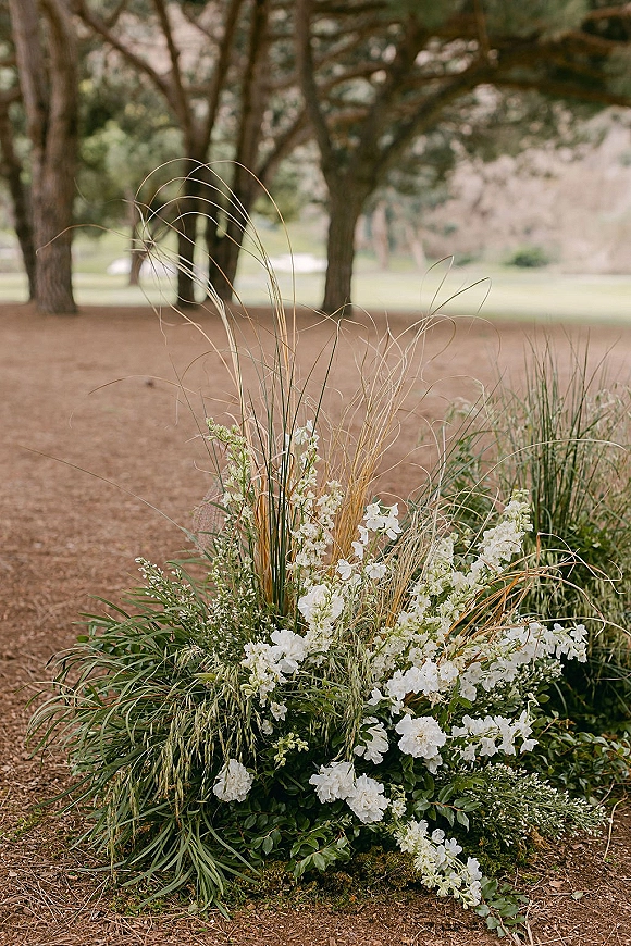 Wedding floral arrangement with white flowers and greenery, set as a ground floral arrangement on moss in a tree grove ceremony area