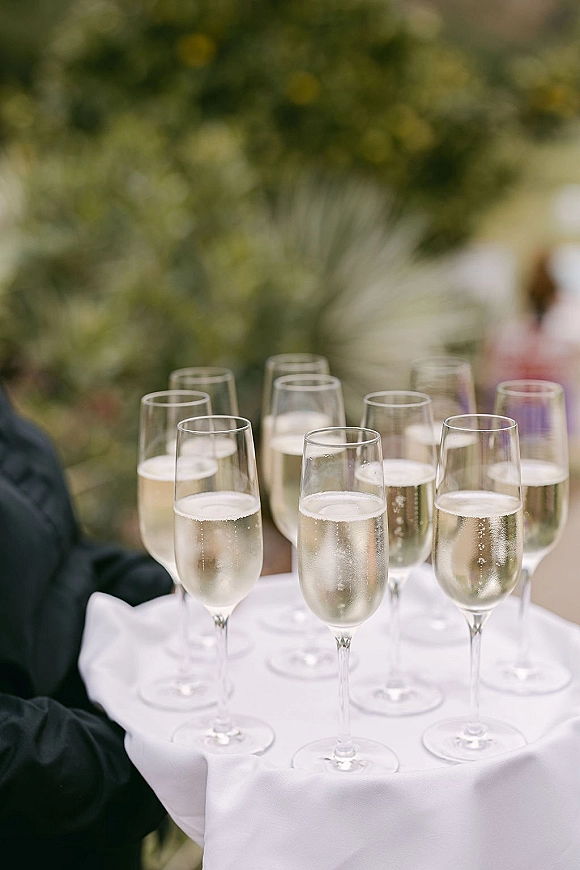 Champagne toast tray with wedding champagne service, gloved hands holding flutes on a white napkin against lush garden greenery
