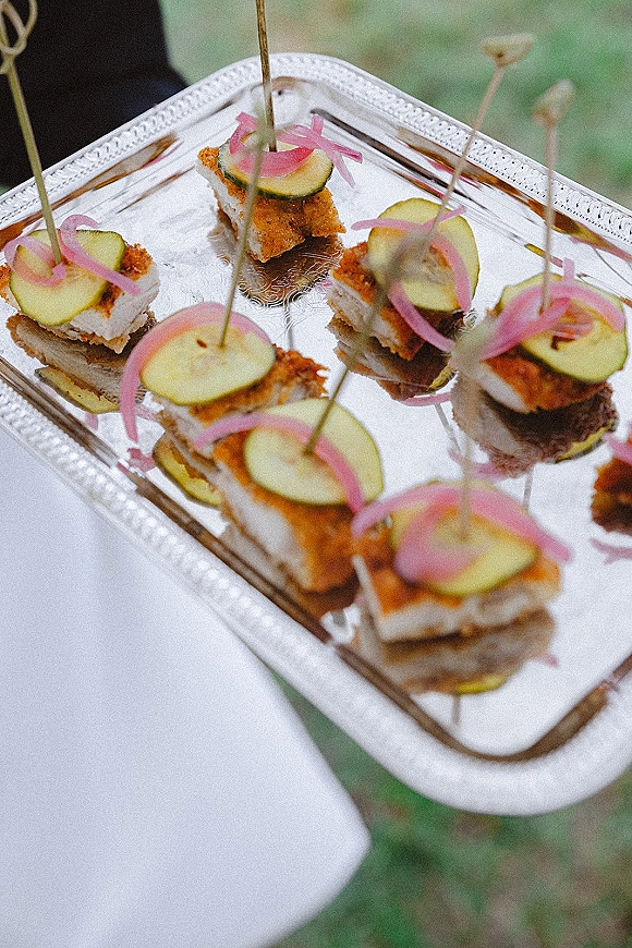Wedding appetizers and passed hors d'oeuvres arranged on a silver serving tray with cocktail picks, cucumber slices, and pickled onions on grass