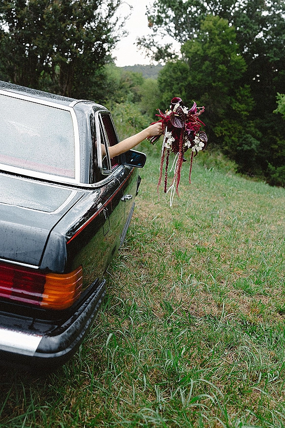Bridal bouquet, burgundy bridal bouquet with cascading calla lilies and trailing ribbon held from a vintage car window in an overcast field