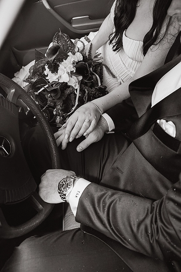 Wedding couple portrait of bride and groom in car holding hands, bouquet of calla lilies and orchids on lap, ring and watch visible
