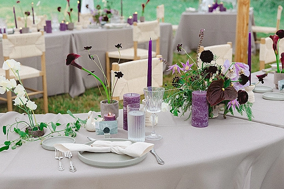 Reception tablescape with purple wedding tablescape details—gray linens, lavender taper and pillar candles, floral centerpieces, set under an outdoor tent