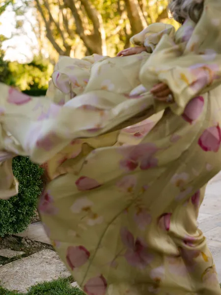 Bridesmaid dress in yellow floral print with puff sleeves and a statement ring, worn on a stone garden path amid greenery