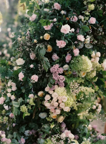 Wedding floral installation with ceremony floral backdrop of roses, hydrangea, and greenery in soft outdoor garden light