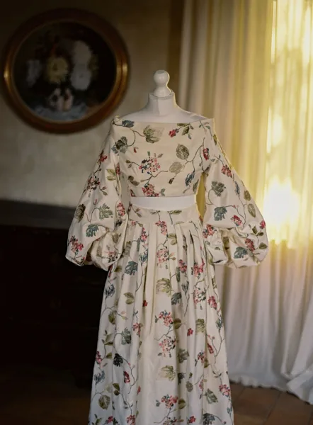 Wedding dress with floral wedding dress print on a mannequin, long puff sleeves and satin waistband glowing in soft window light near sheer curtains