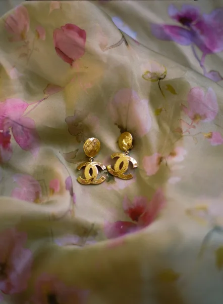 Bridal earrings in gold bridal earrings style, set on sheer floral fabric with designer logo detail against softly draped textile background