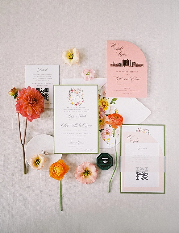 Wedding invitation suite with colorful wedding invitations, RSVP and QR code cards, rings in velvet box, and floral accents on linen backdrop