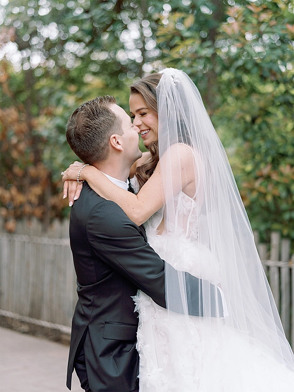 Wedding couple portrait of bride and groom hug on an outdoor path, bride in strapless gown with veil smiling as groom kisses her forehead