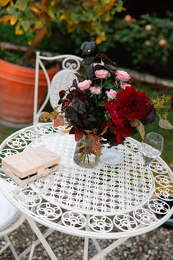 Reception tablescape with a garden reception table centerpiece in a glass vase of pink roses and red dahlia on a white wrought iron table outdoors