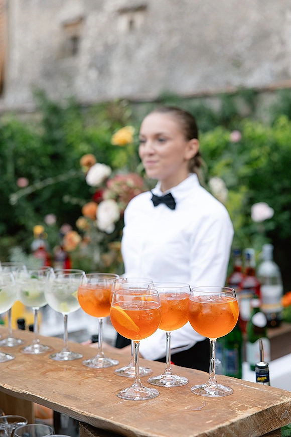 Wedding cocktail bar with signature wedding cocktails in chilled glasses, citrus slices and ice on a wooden counter, foliage backdrop