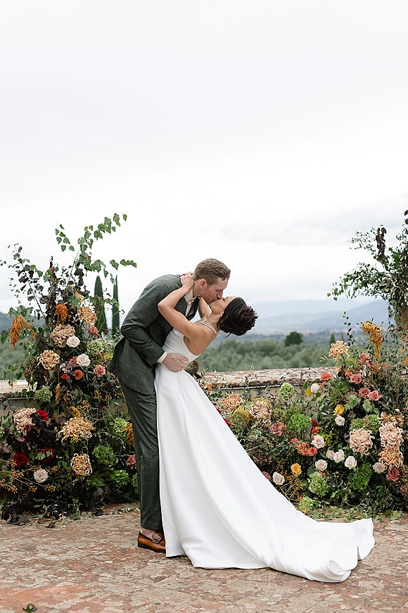 Wedding kiss portrait of the bride and groom kiss in a dip on a stone terrace, her long train flowing with mountain views behind