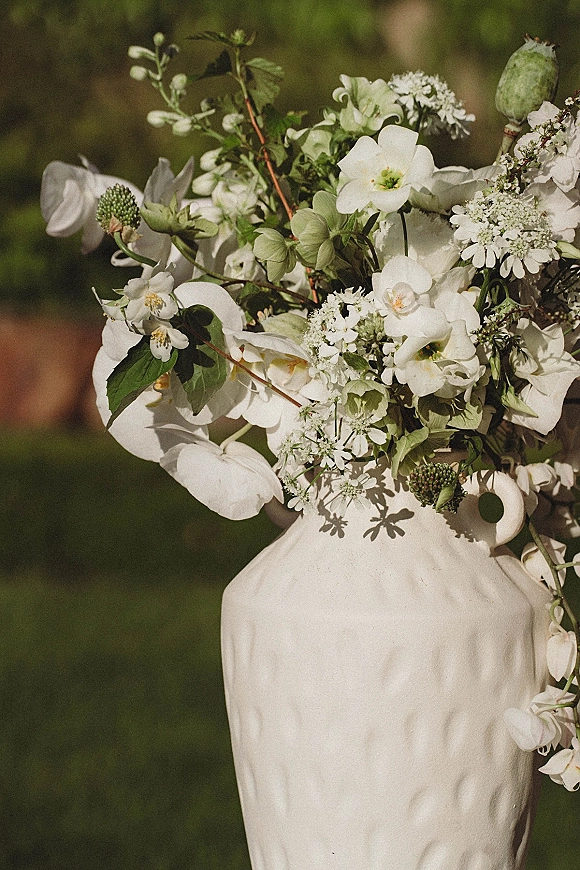 Wedding cake with white floral wedding cake details, textured buttercream tiers, sugar flowers and greenery in a blurred garden backdrop