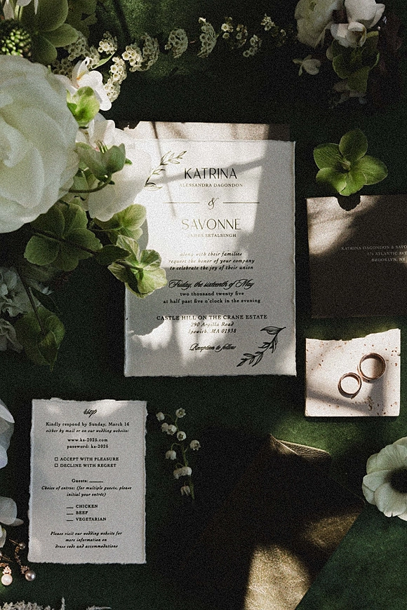 Invitation suite wedding invitation flat lay with RSVP card, envelope and wax seal, rings and pearls amid greenery on dark fabric with sun shadows
