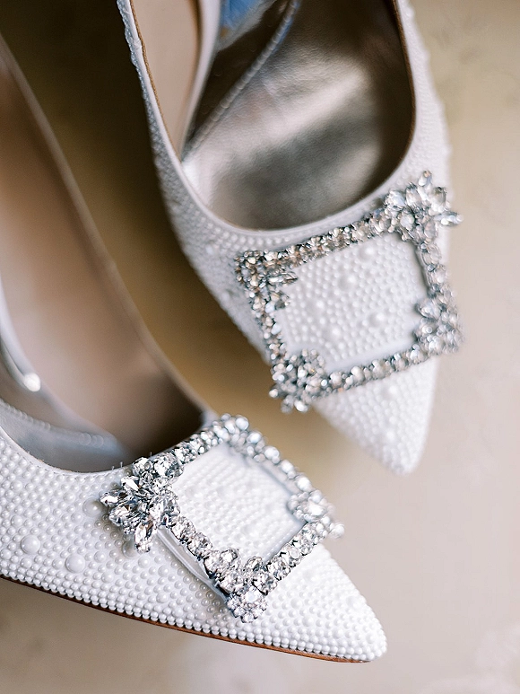 Bridal shoes in a wedding shoes flatlay with pearl beading and a crystal buckle, resting on a smooth neutral surface