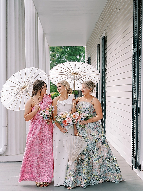Bridesmaid portrait of bride with bridesmaids holding paper parasols and bouquets on a white porch with columns and black shutters