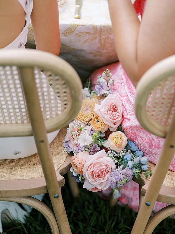 Wedding bouquet in pastel wedding bouquet tones with garden roses, ranunculus, and lavender blooms on a wooden bistro chair at outdoor table