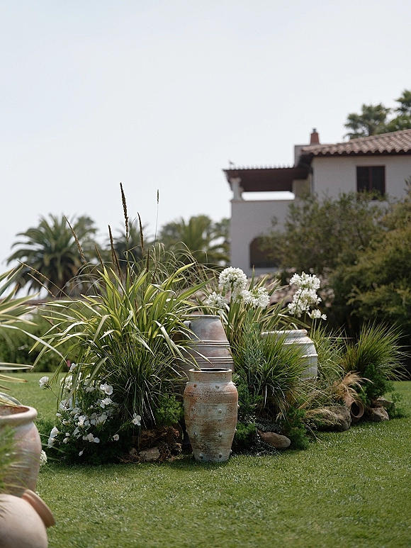 Ceremony aisle decor with aisle floral meadow in ceramic urns and vases, white flowers and grasses edging a lawn near a stucco building