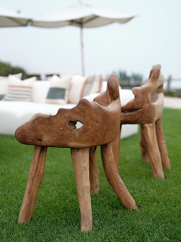 Wedding lounge seating with an outdoor sofa and throw pillows under a patio umbrella on a grass lawn with open sky backdrop