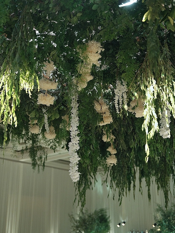 Hanging floral installation with ceiling greenery installation, cascading foliage and white garlands beneath a white draped ceiling