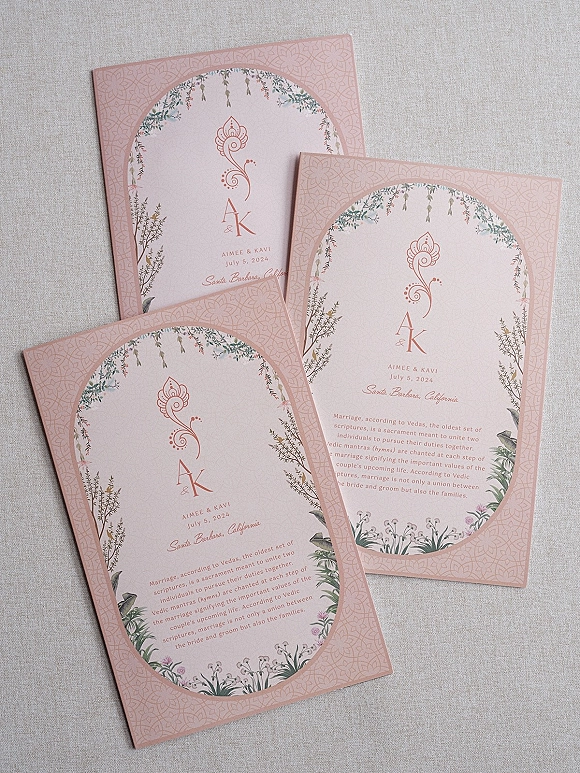 Wedding invitations in a wedding invitation suite with arched pastel pink cards, monogram initials and floral border on linen backdrop