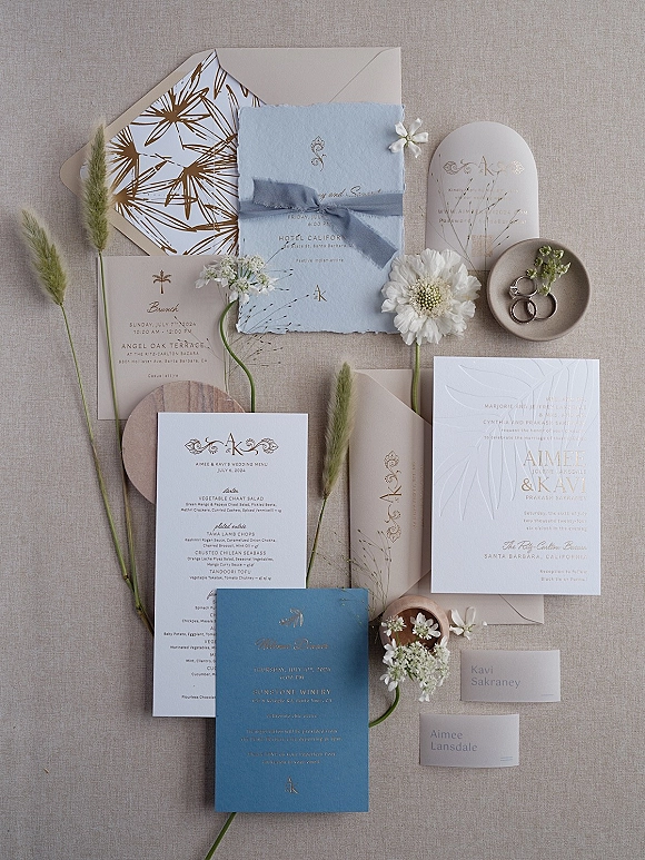 Invitation suite wedding invitation flat lay with deckled cards, ribbon and wax seal, floral sprigs, place cards, and rings on linen backdrop