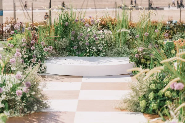 Ceremony altar decor on a round wedding altar with meadow florals, allium and grasses, beside a checkered aisle runner on an outdoor walkway