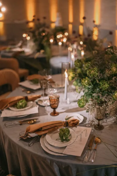Reception tablescape with wedding table decor, taper candles and greenery garland with floral centerpieces in a warmly lit reception room