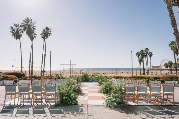 Ceremony setup for a beach wedding ceremony with striped aisle runner, wood chairs, and lush ground florals facing the ocean and palms