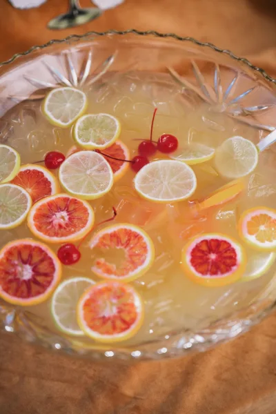 Wedding punch bowl filled with ice and citrus slices, with blood orange garnish and a ladle resting inside on a wood table