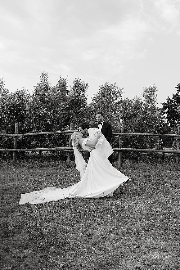 wedding kiss portrait of groom dipping bride in strapless gown with long train and veil, kissing on a grassy lawn by a wooden fence