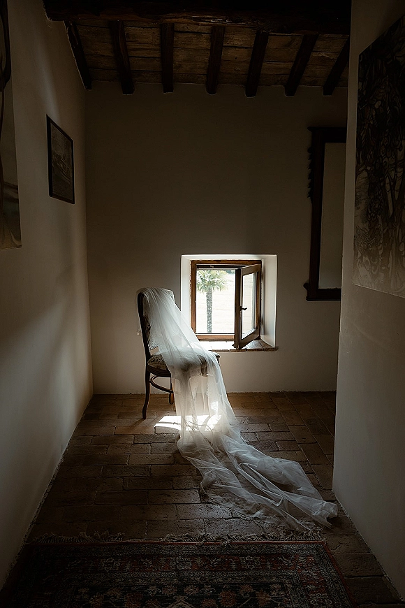 Bridal veil with cathedral veil train draped over a chair by an open window, sheer tulle in soft light, wood beams above