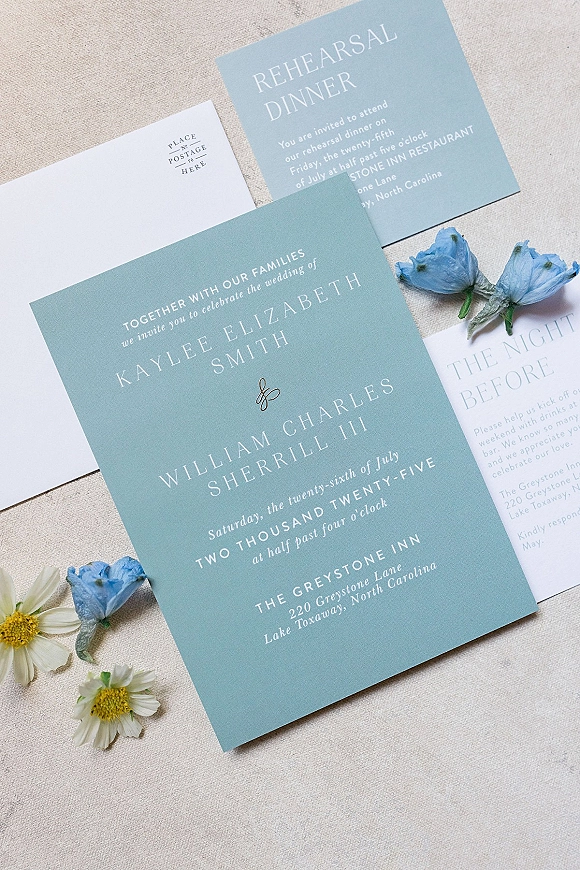 Wedding invitation suite with blue wedding invitations, envelopes, rehearsal dinner and details cards, gold monogram and flowers on linen fabric