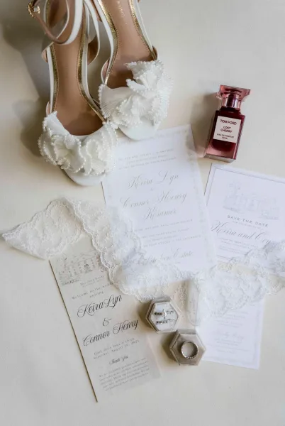 Invitation suite with wedding invitation suite cards, lace accent, bridal shoes, perfume bottle, and velvet ring boxes on a neutral tabletop