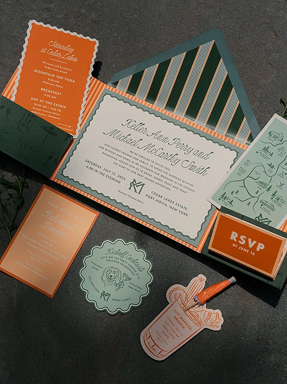 Invitation suite wedding invitation set with orange and green calligraphy cards and striped envelope liner on stone with greenery sprigs