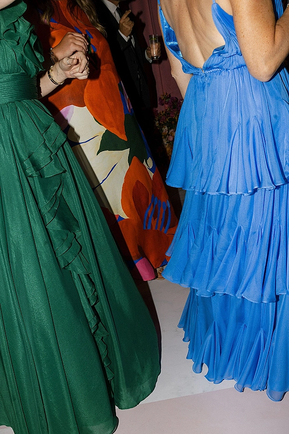 Wedding guest outfits in colorful wedding guest dress styles, with ruffled blue and green dresses and floral prints on an indoor dance floor