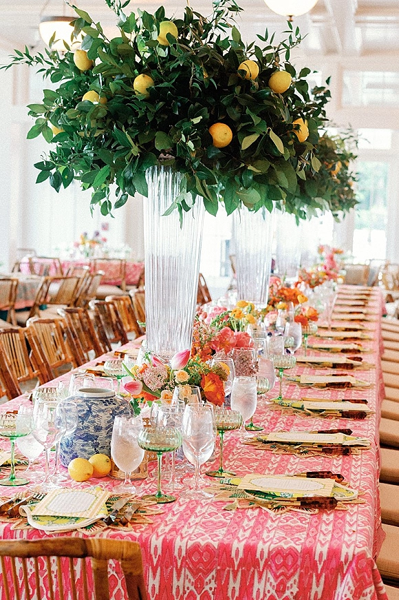 Reception tablescape with wedding reception table decor on a pink patterned tablecloth, citrus greenery and tall vase centerpieces in a bright indoor venue