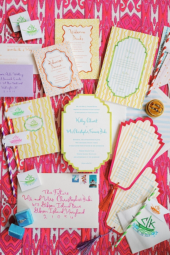 Invitation suite with colorful wedding invitations, RSVP and reception cards, calligraphy envelopes, monogram stickers, and rings on pink fabric