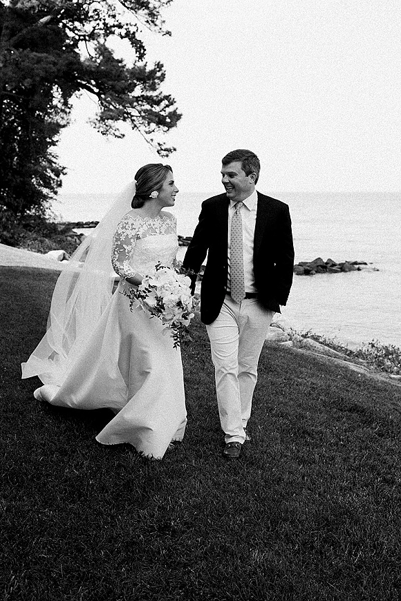 Couple portrait in a black and white wedding portrait style, bride in veil and lace sleeves holding bouquet beside groom on rocky shore