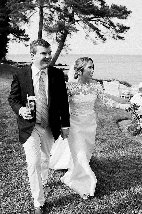 Couple portrait, black and white wedding photo of bride in lace gown and veil holding bouquet beside groom with drink on ocean lawn
