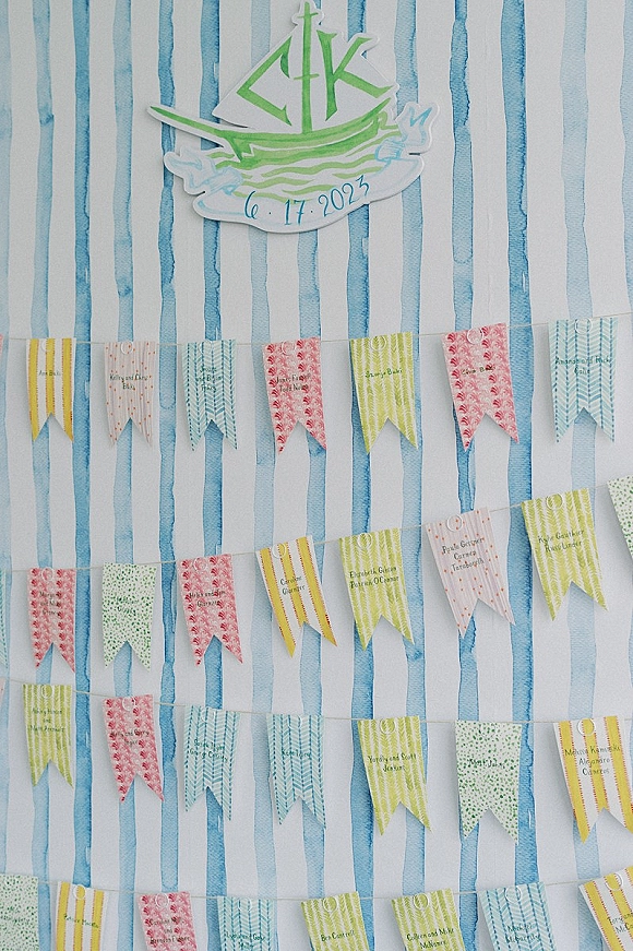 Wedding seating chart with paper pennant flags on twine, printed guest names, and a nautical sailboat sign against blue-white stripes