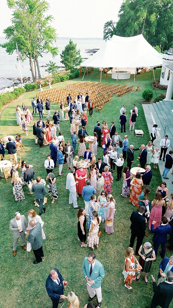 Wedding cocktail hour with guests mingling around cocktail tables and drinks under a white tent canopy on an oceanfront lawn