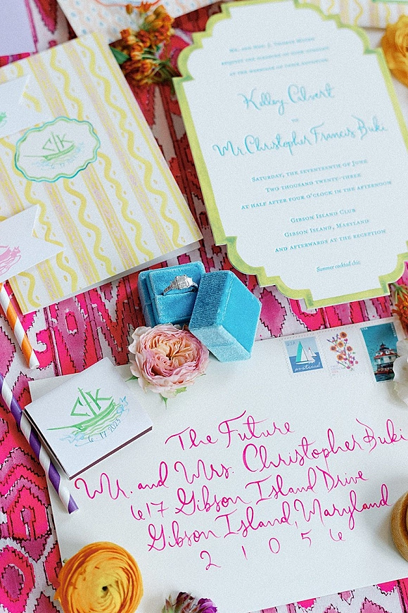Invitation suite with colorful wedding invitations, modern calligraphy envelope, stamps, monogram seal and ring box on pink patterned textile backdrop